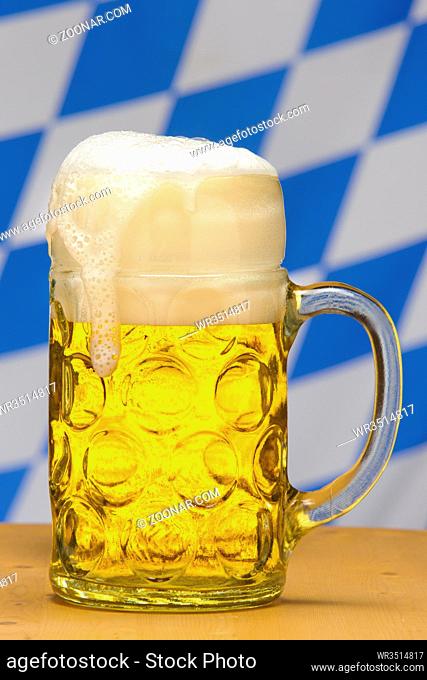 big glass filled with Bavarian lager beer and flag of Bavaria in background
