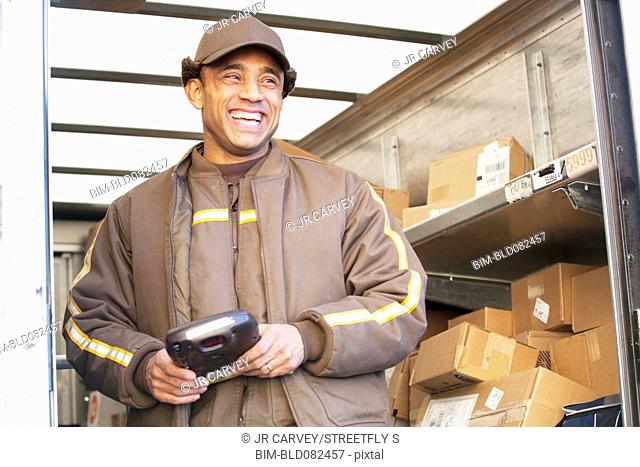 Smiling Hispanic delivery man standing in back of truck