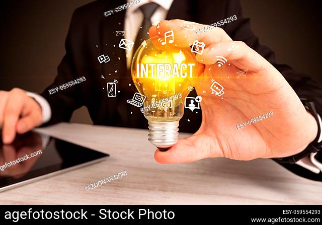 Businessman holding light bulb with INTERACT inscription, social media concept
