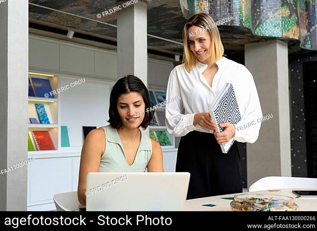 Mid-shot of female Latin-American interior designer and her assistant looking at laptop computer screen