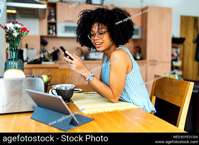 Female entrepreneur with curly hair using smart phone at desk in home office