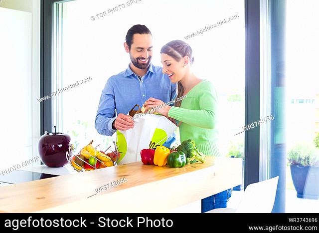 Man and woman unpacking fruits and vegetables out of grocery shopping bag in home kitchen