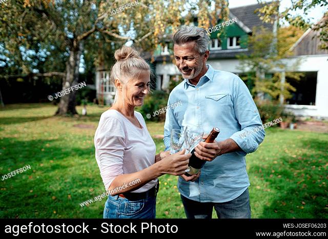 Smiling couple holding champagne bottle and flute at backyard