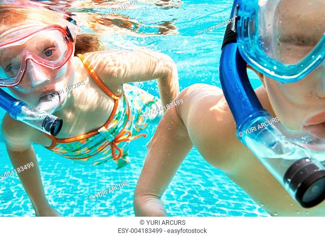 Portrait of two children playing underwater in the pool wearing snorkels