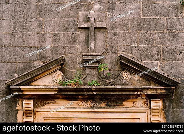 Gray wall with a cross carved into the stone in the style of a bas-relief, above the entrance to the building. High quality photo