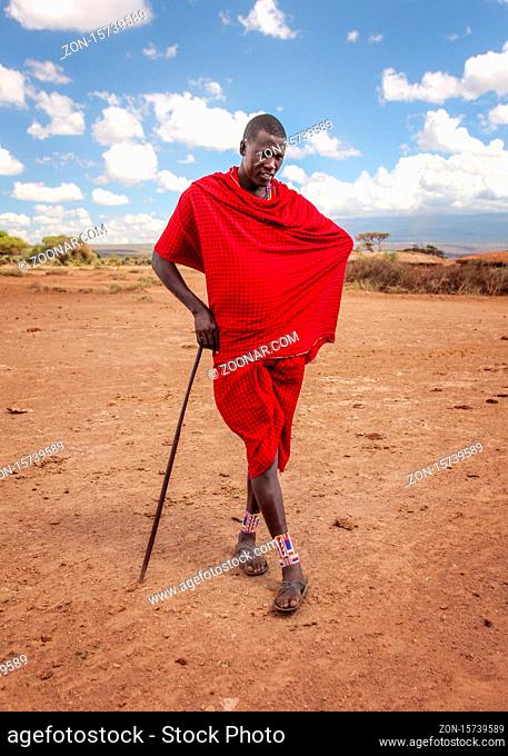 Unknown village near Amboselli park, Kenya - April 02, 2015: Unknown Masai warrior posing for tourists in traditional bright red robe, leaning on his stick