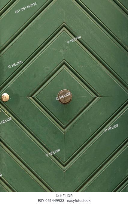 A green painted wooden door with diamond pattern, round door knob and mail slit