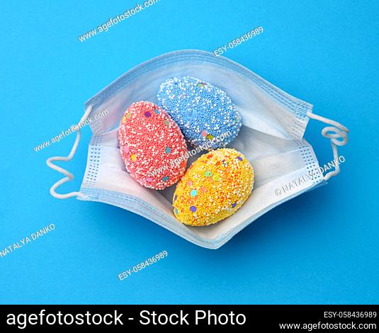 decorative easter eggs lie in a disposable medical mask on a blue background, top view