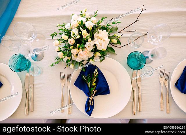 White plates with blue cloth napkins. Glass glasses, blue candles, floral arrangement in the center of the table