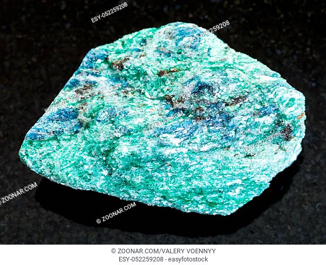 macro shooting of natural mineral rock specimen - rough Fuchsite (chrome mica) stone on dark granite background from Hizovaara, Republic of Karelia in Russia