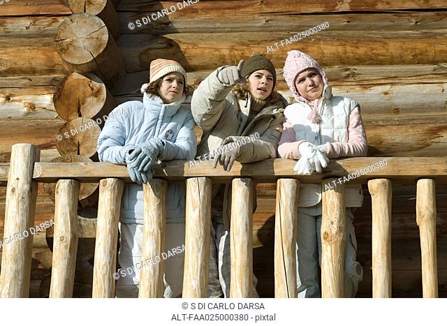 Three preteen or teen girls standing on deck of log cabin, looking away, low angle view