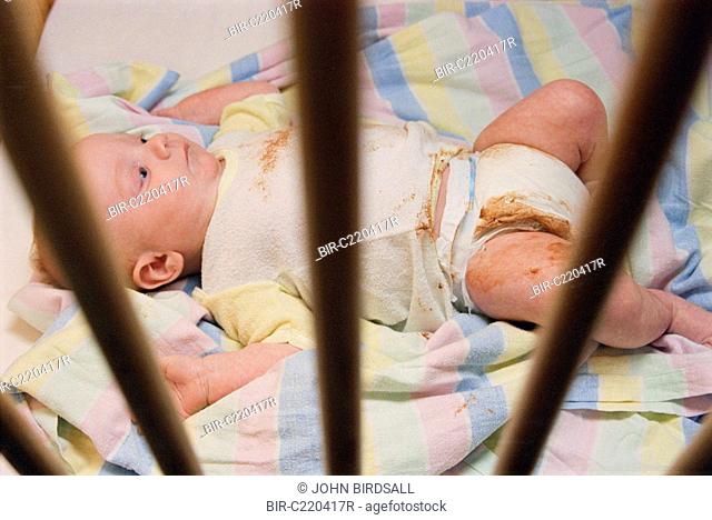 Neglected baby lying in dirty cot wearing soiled nappy
