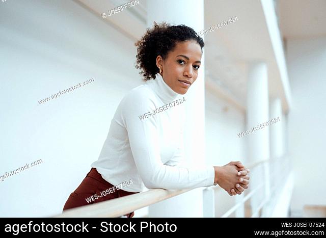 Businesswoman with hands clasped leaning on railing in corridor