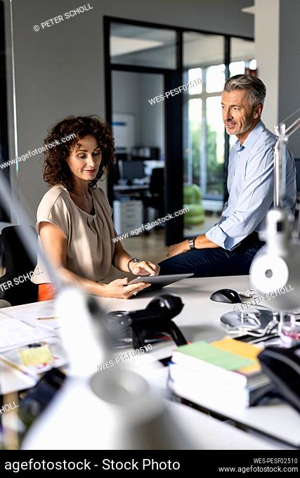 Mature businesswoman explaining over digital tablet to colleague while sitting at office