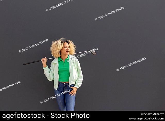 Smiling woman with golf club standing in front of black wall