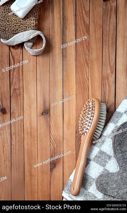 Accessories for visiting a bath or sauna on a wooden background: towel, washcloth, massage brush, soap, glove. Top view with copy space. Flat lay