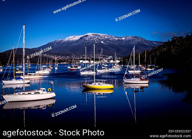 Boats and reflections in Lindisfarne, Hobart, Tasmania, Australia in winter with view on Mount Wellington covered in snow