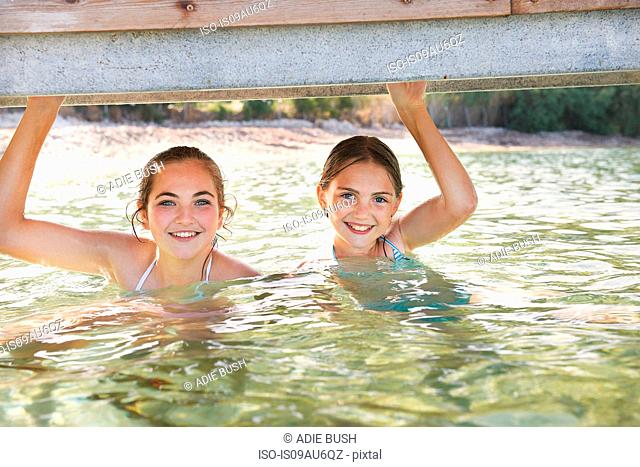 Portrait of two girls in sea holding onto pier