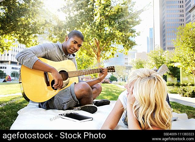 Man playing guitar for girlfriend in park