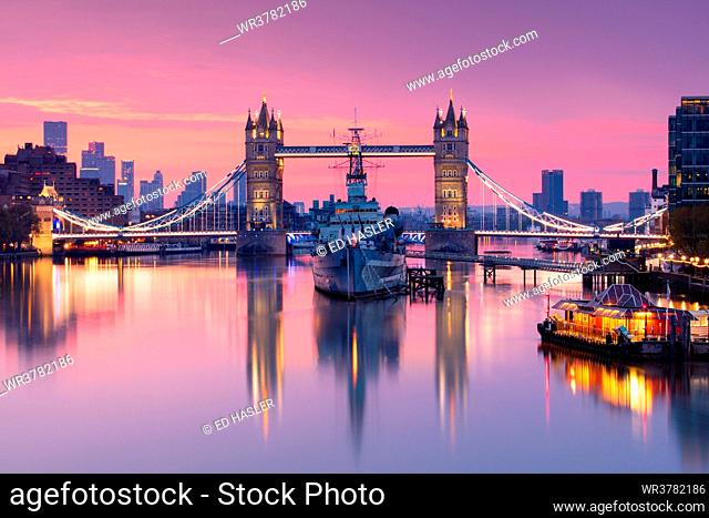 Sunrise view of HMS Belfast and Tower Bridge reflected in River Thames, with Canary Wharf in background, London, England, United Kingdom, Europe