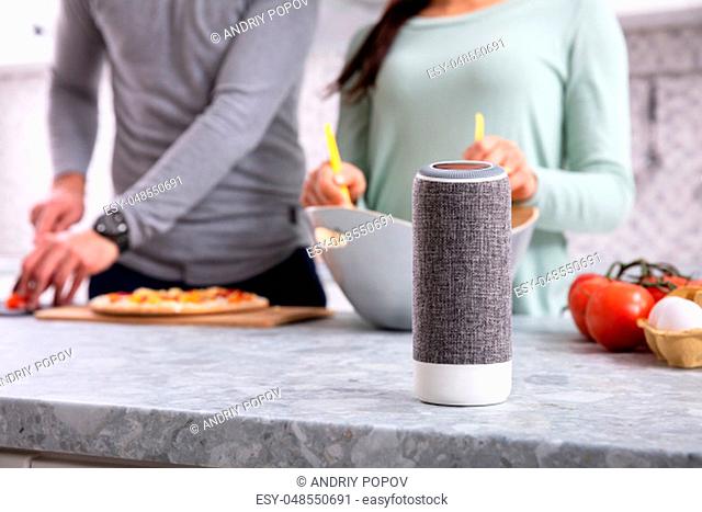 Close-up Of Wireless Speaker In Front Of Couple Preparing Food In Kitchen