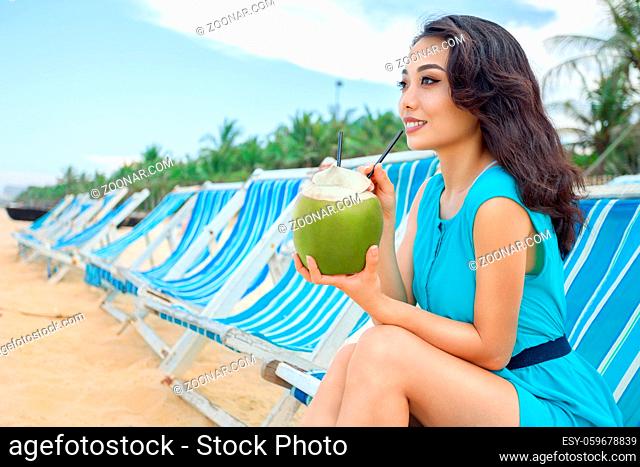 Young beautiful asian woman is drinking coconut juice on the tropical sea beach