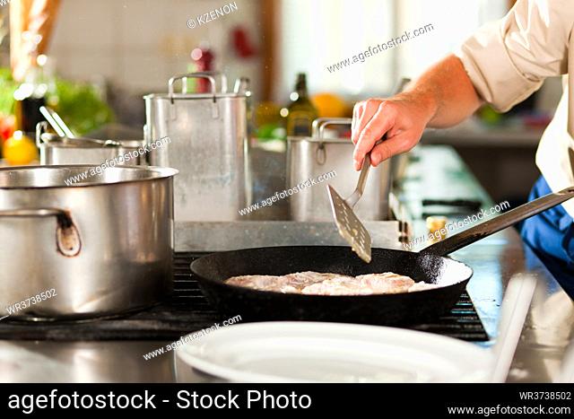 Close up of chefs in a commercial restaurant or hotel kitchen working, they are preparing an fish fillet