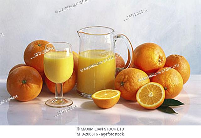 Orange Juice in a Glass and Pitcher, Surrounded by Fresh Oranges