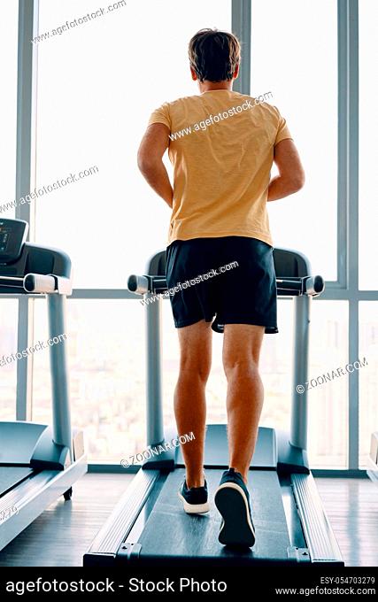 Full length portrait of young sports man running on a treadmill at gym. Fitness, workout and and healthy lifestyle concept. Full length