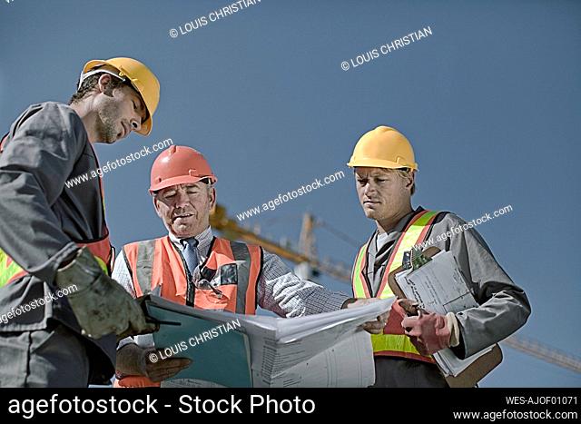 Male construction worker discussing with coworkers at construction site against clear sky