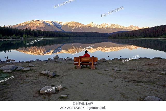 Middle age male sitting on bench looking Patricia Lake, Jasper National Park, Alberta, Canada