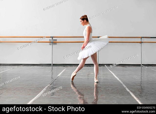 Beautiful female ballet dancer in ballet class, barre and white wall on background