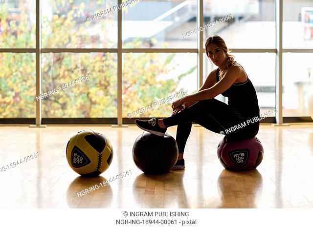 Woman sitting with fitballs in the gym. Young female wearing sportswear clothes