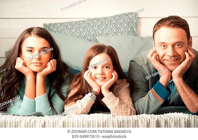 Family portrait of happy parents and their daughter laying on bed at home