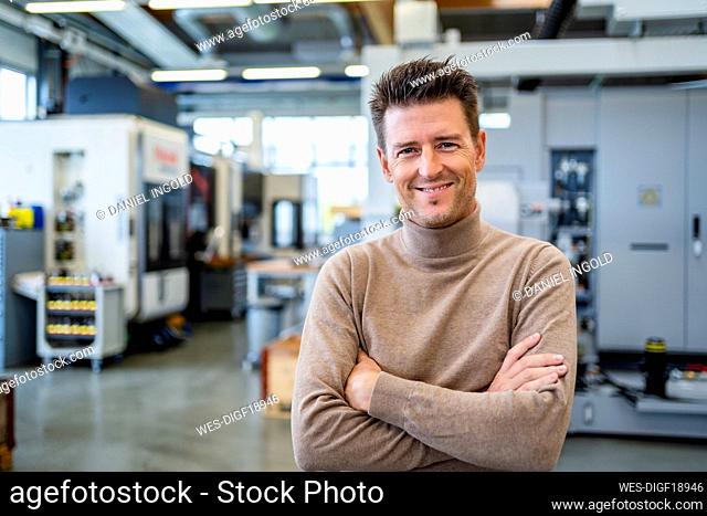 Smiling mature businessman with arms crossed in industry