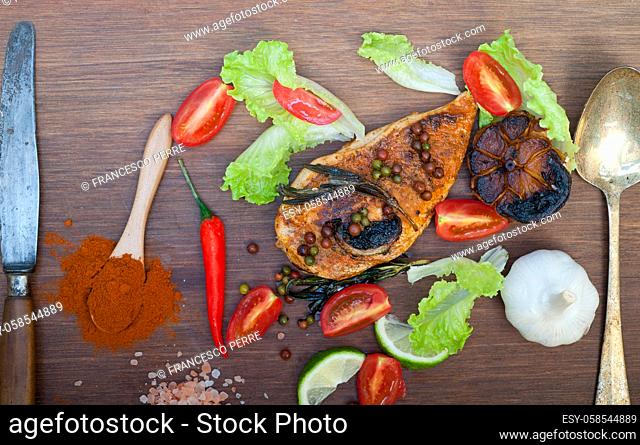 wood fired hoven cooked chicken breast on wood board with herbs spices and vegetables