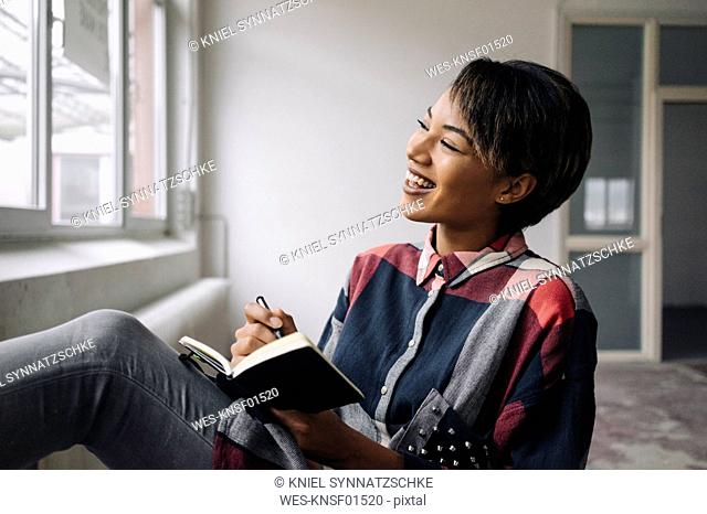 Smiling woman sitting at the window with notebook