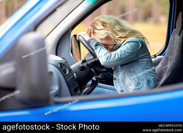 Woman with blond hair resting on steering wheel in van