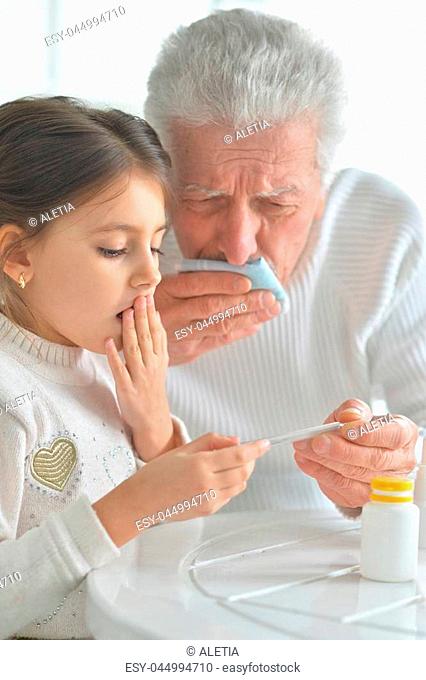 Sad granddaughter and her sick grandfather looking at thermometer together