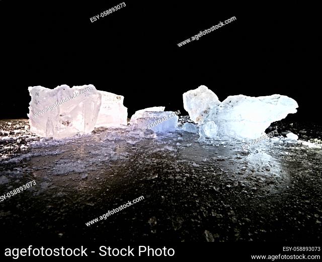 Melting pieces of chopped ice blocks. Strong colorful backlight shine deep cracks, low angle view. Far flat horizon