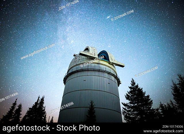 Rozhen astronomical observatory under the night sky stars. Blue sky with hundreds of stars of the Milky way. Observatory in a pine trees forest in the mountain