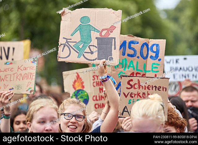 11 August 2023, Lower Saxony, Lüneburg: A participant in a protest march of the climate movement Fridays for Future carries a cardboard sign with a depiction of...