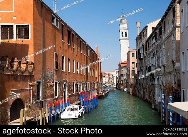 Moored boats and water taxi on narrow canal and old architectural style residential buildings, leaning church bell tower, San Marco, Venice, Veneto, Italy