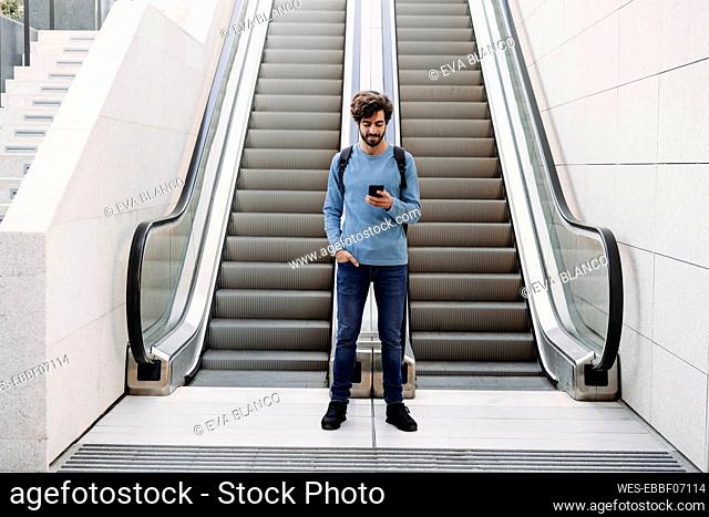 Young man using smart phone standing in front of escalator