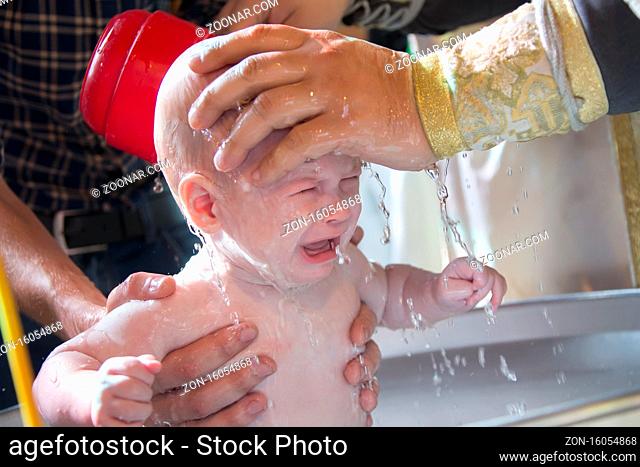 Priest pours water on the infant at baptism. Orthodox rite of baptism. Acceptance of faith. Child in the font