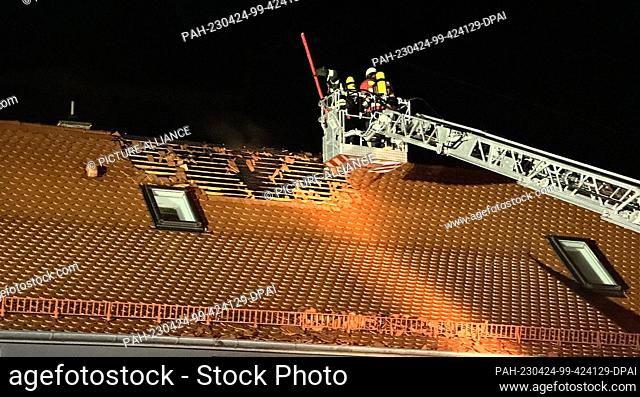 23 April 2023, Bavaria, Muhr Am See: Firefighters work in an aerial ladder above a roof. A 13-year-old boy and two adults were slightly injured when lightning...