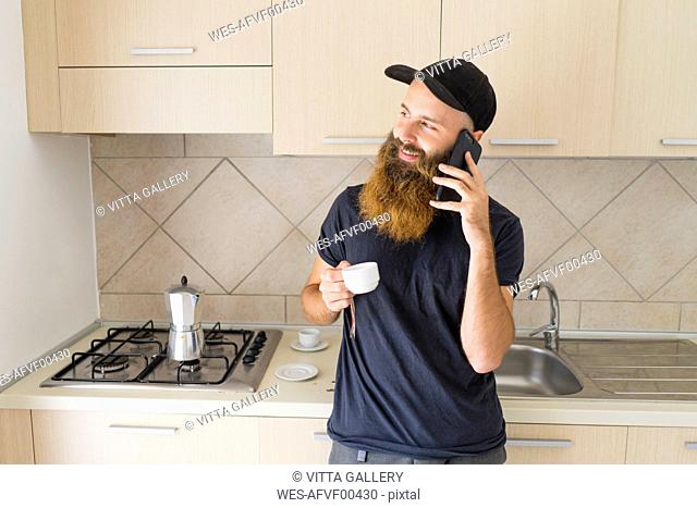 Portrait of bearded man on the phone standing in kitchen with espresso cup