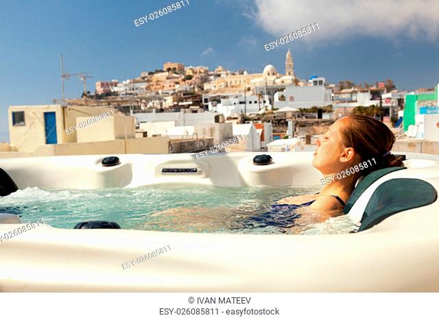 Young woman enjoying outside jacuzzi. In background - the center of Fira, Santorini