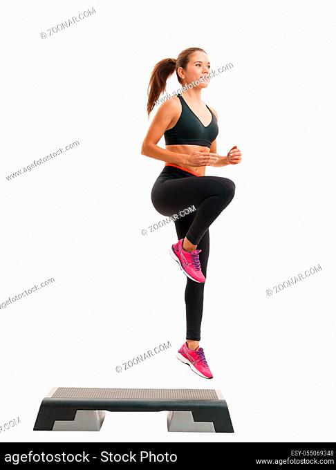 Step-aerobics, fitness and shaping concept - young energetic sporty woman in sportswear exercising with stepper on white isolated background