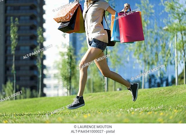 Young woman running in park, carrying shopping bags
